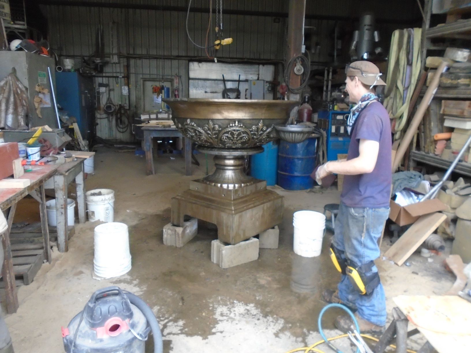 Person in a workshop beside a large ornate metal fountain on a wheeled base