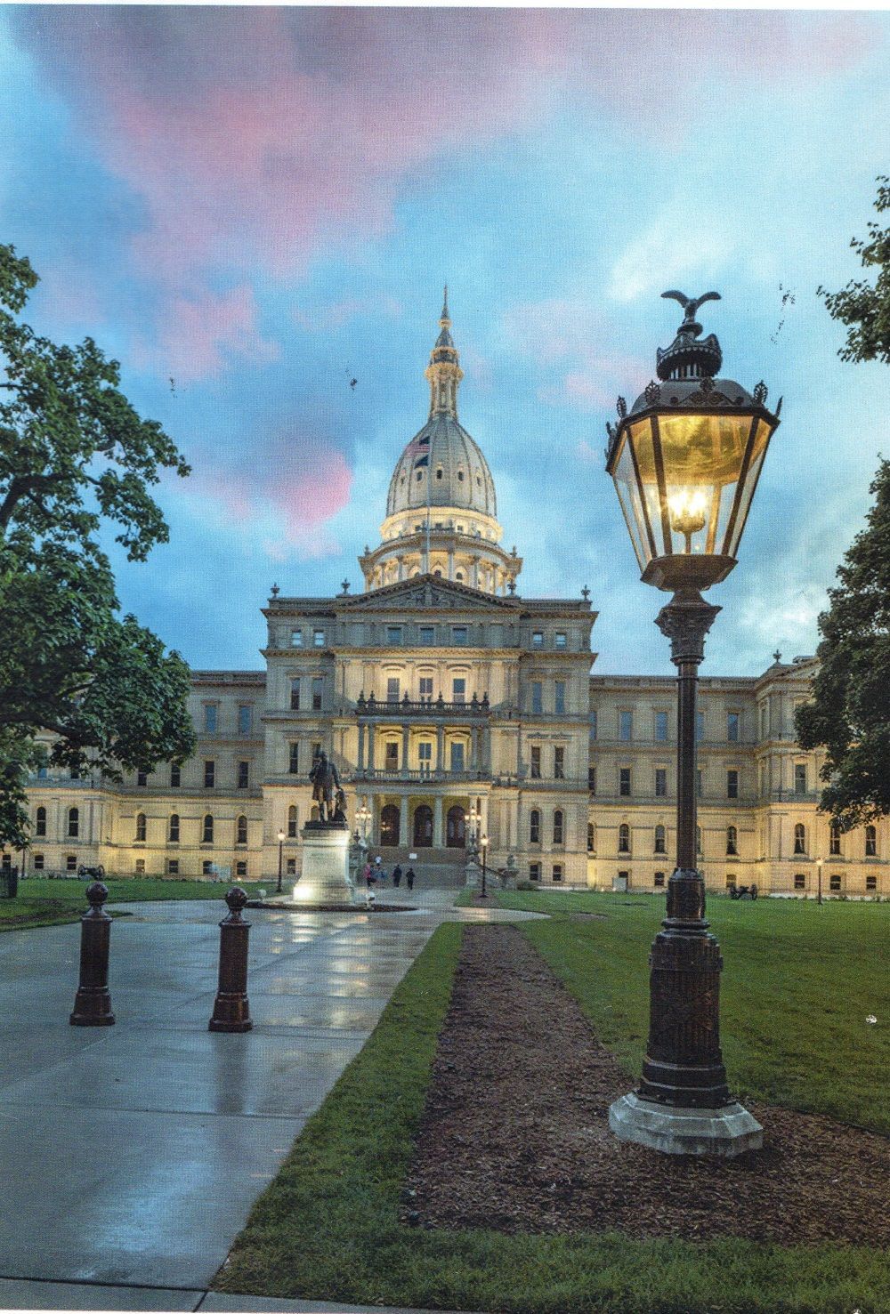 Historic capitol building at dusk with a lit streetlamp and wet path in the foreground