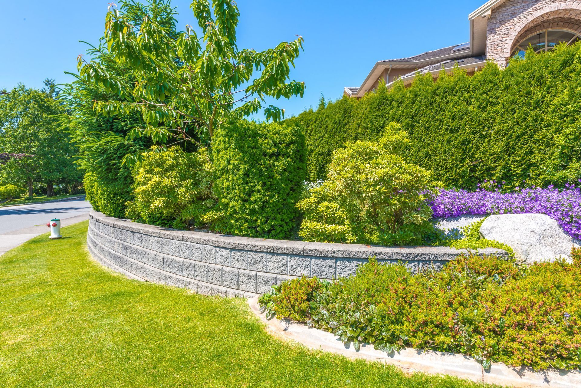 Stone retaining wall with lush greenery and flowers. Sunny day.