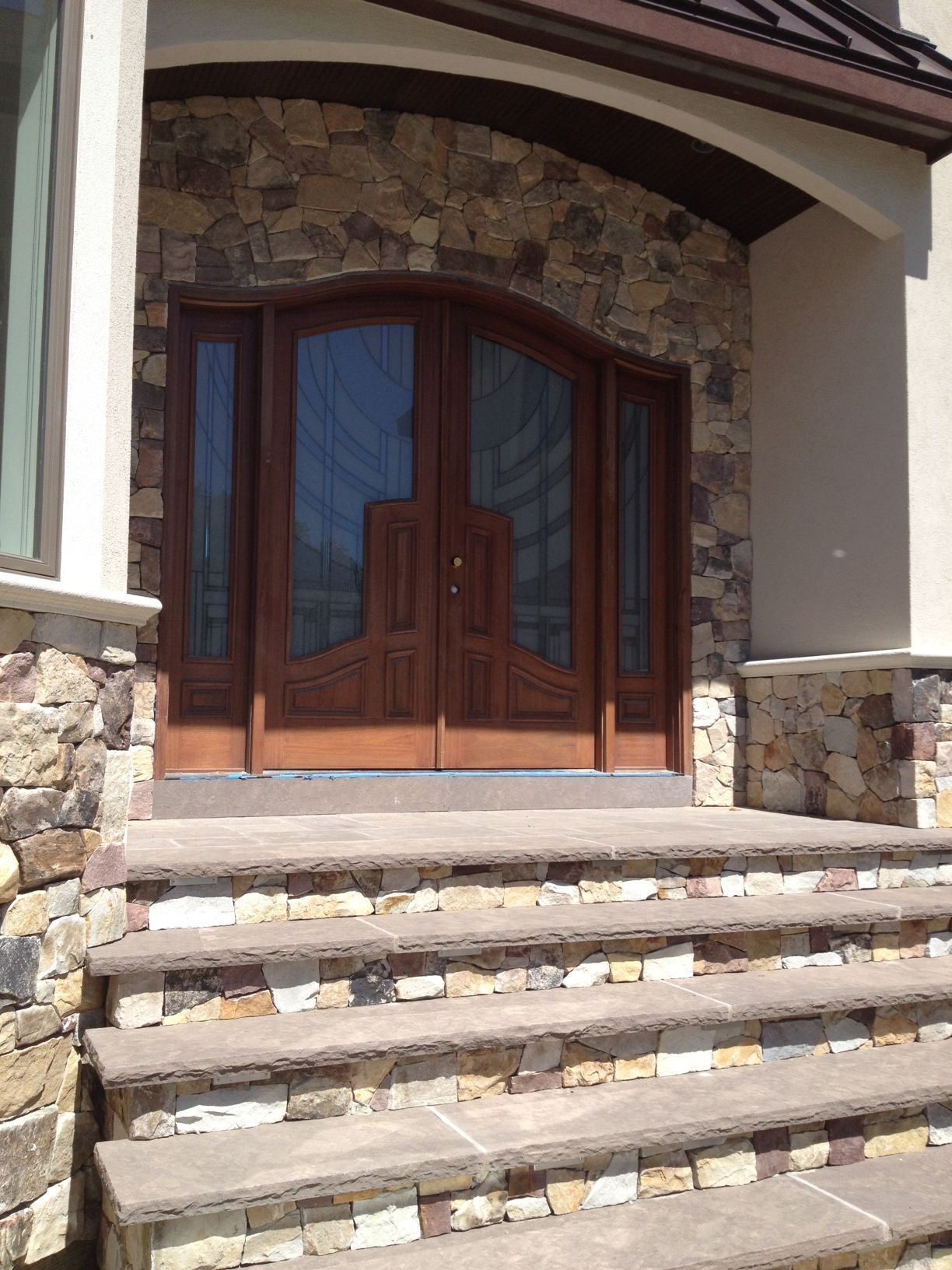 Stone steps leading to a wooden double door entrance with glass panels and stone facade.