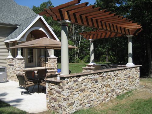 Outdoor kitchen area with stone walls, pergola, and dining set.