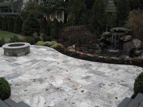 Stone patio with fire pit and waterfall feature surrounded by landscaping.