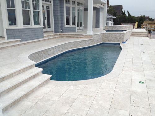 Outdoor swimming pool with stone deck and stairs next to a house with blue siding.