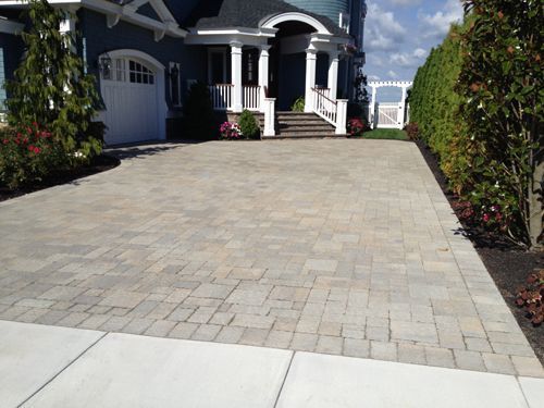 Brick paver driveway leading to a blue house with white trim and a white garage door.
