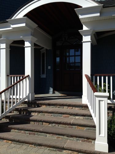 Stone steps lead to a dark brown door framed by white pillars and railing.