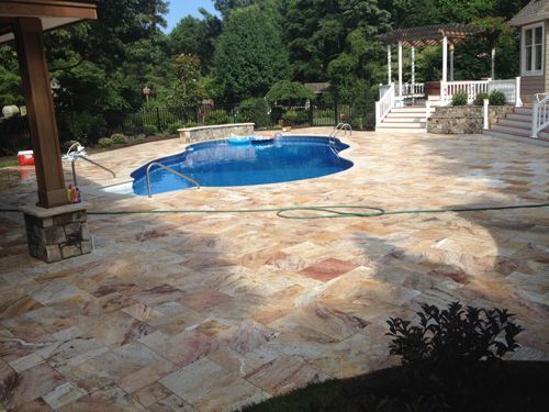 Pool and patio area with blue water, beige stone tiles, and a white gazebo.