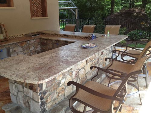 Outdoor bar with stone facade and granite countertop, with seating and decorative tile accents.