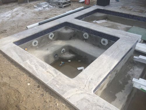 Two adjacent, unfinished spas with tile edging and exposed plumbing fixtures, under construction outdoors.