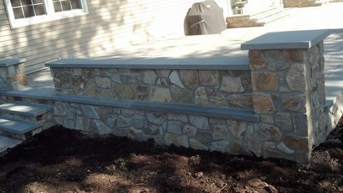 Stone retaining wall and steps with grey capstones, outdoors.