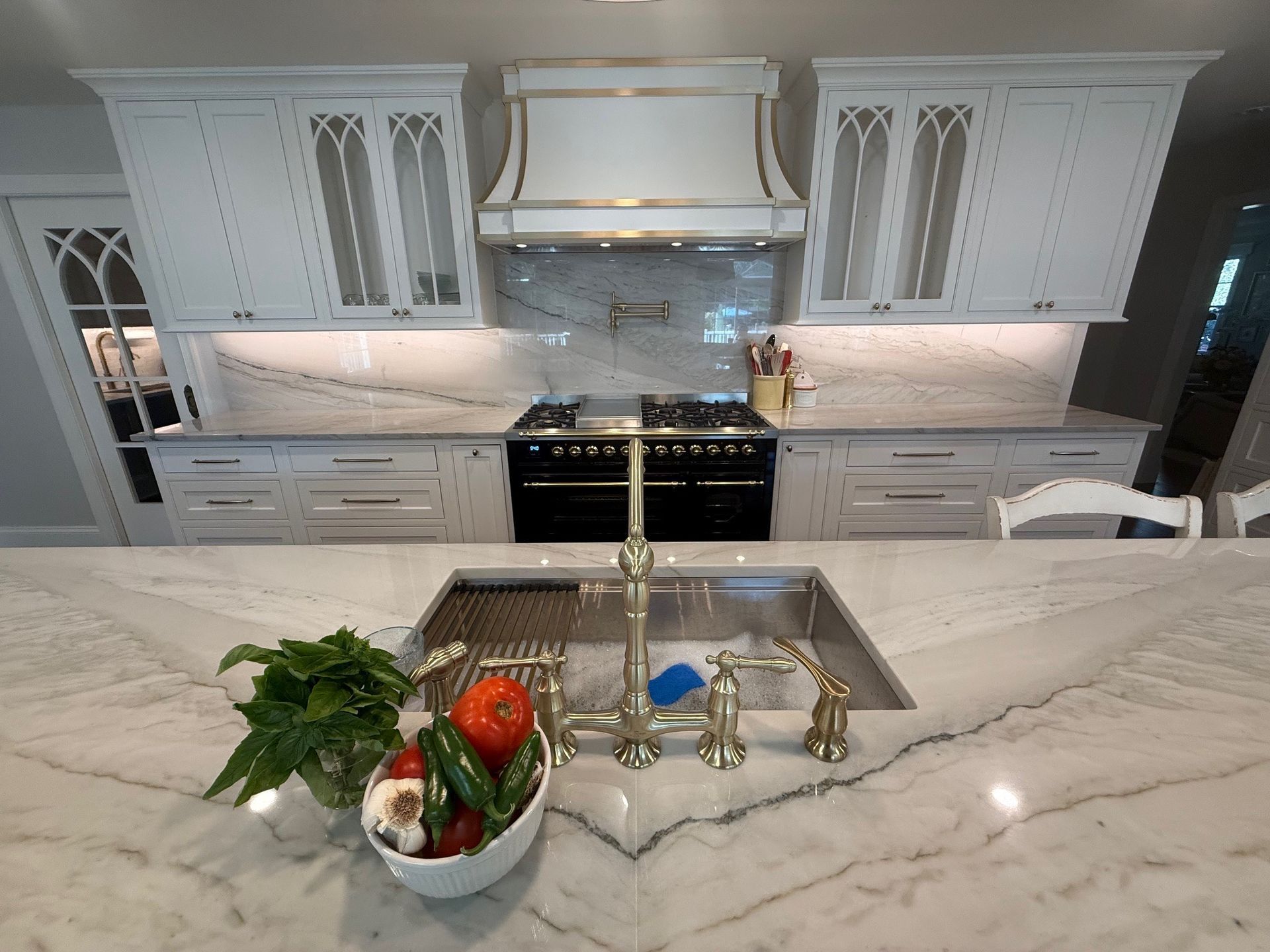 Luxurious white kitchen with marble countertops, stainless steel sink, and a bowl of fresh produce.