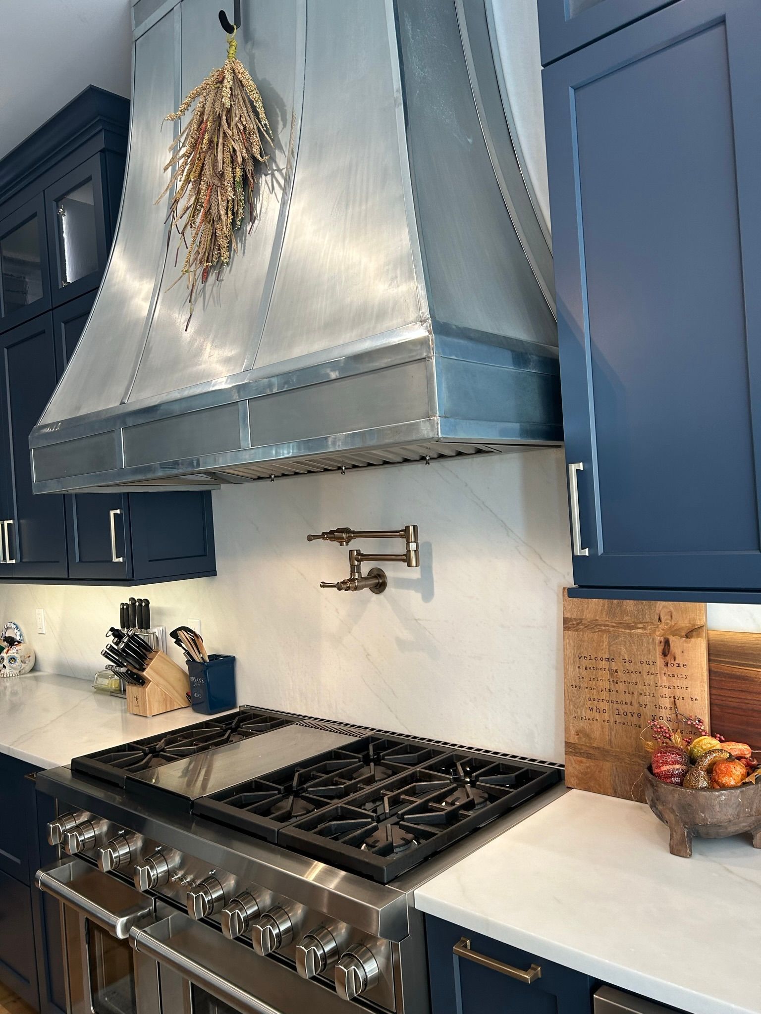 Kitchen with blue cabinets, stainless steel range hood, stove, and white countertop.