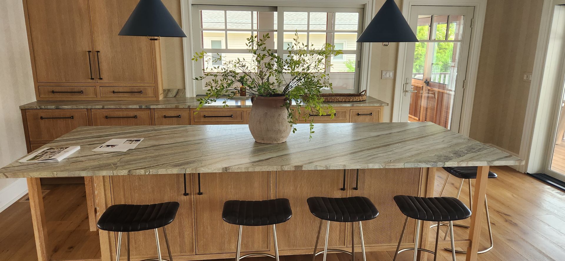 Kitchen with light wood cabinets, granite countertop island, and blue pendant lights.
