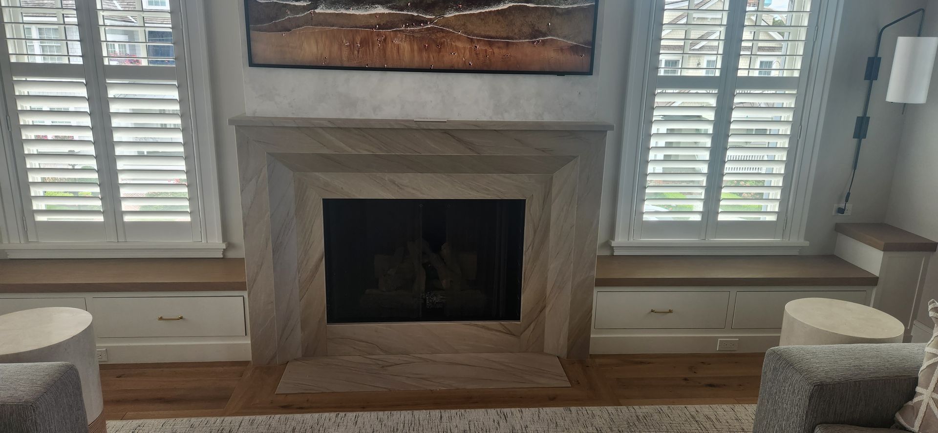 Cozy living room fireplace with stone mantel, shutters, and two upholstered chairs by the windows