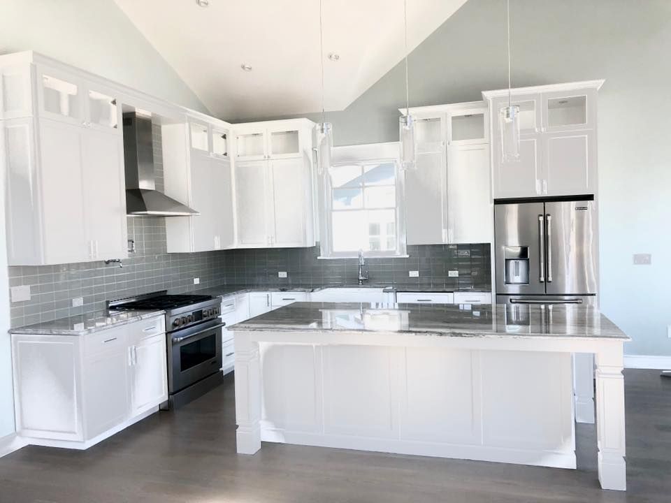 Bright white kitchen with island, stainless steel appliances, and gray backsplash.