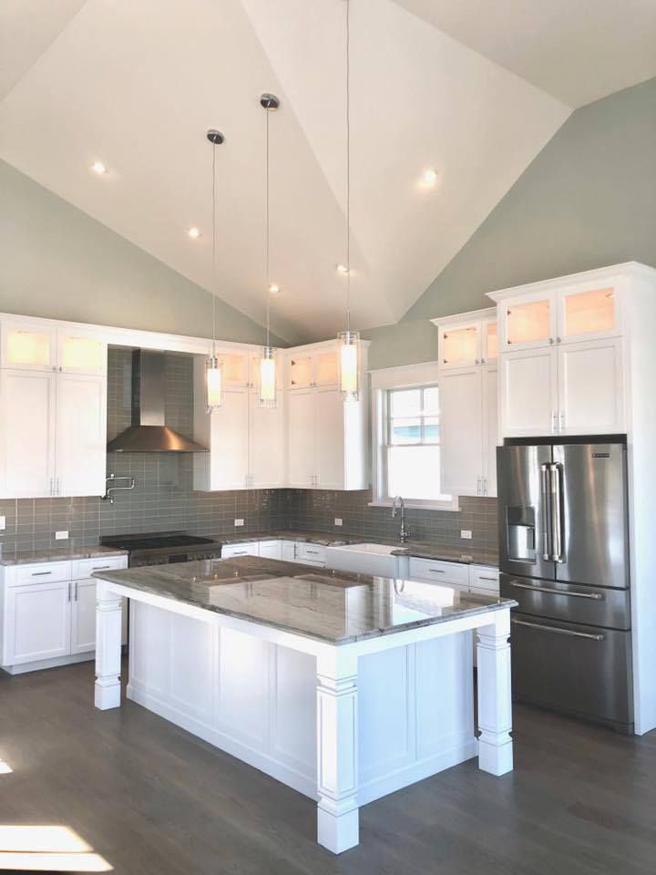 White kitchen with island, stainless steel appliances, and high ceilings.