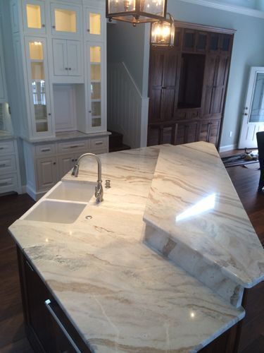 Kitchen island with marble countertop and sink, cabinets, and dark wood flooring.