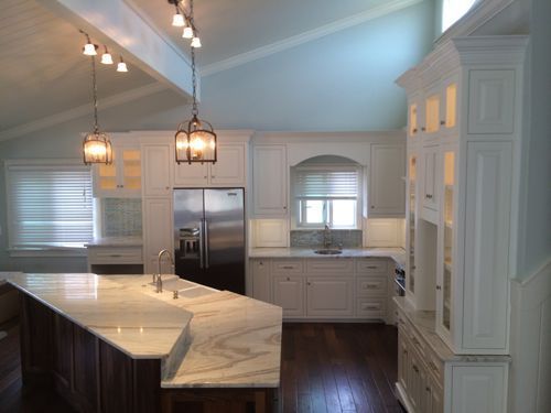 White kitchen with marble countertops, stainless steel appliances, and pendant lights.