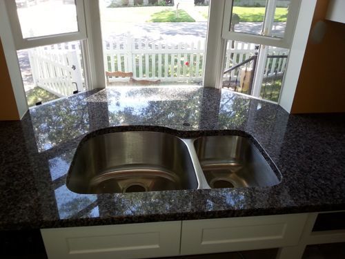 Double sink in dark granite countertop, beneath a window overlooking a white picket fence.