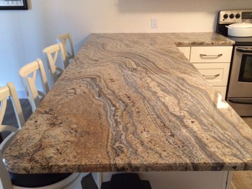 Granite countertop with swirling patterns. White cabinets, chairs visible. Kitchen setting.