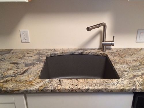 Kitchen sink with granite countertop and stainless steel faucet, set against a cream-colored wall.