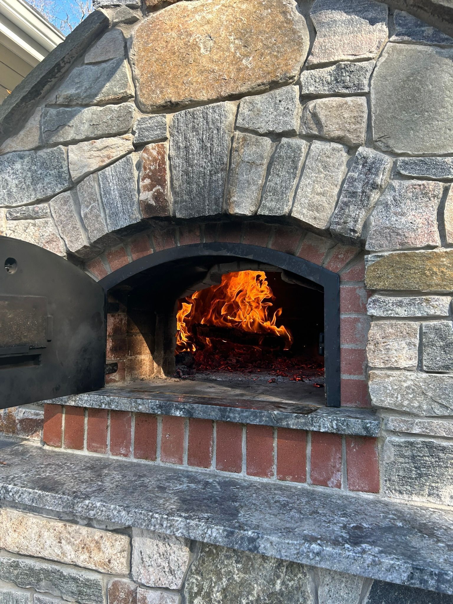 Stone pizza oven with burning wood inside, brick base.