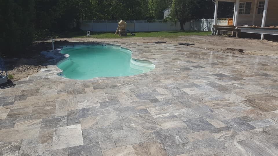Backyard with turquoise pool and stone patio. A person in background.