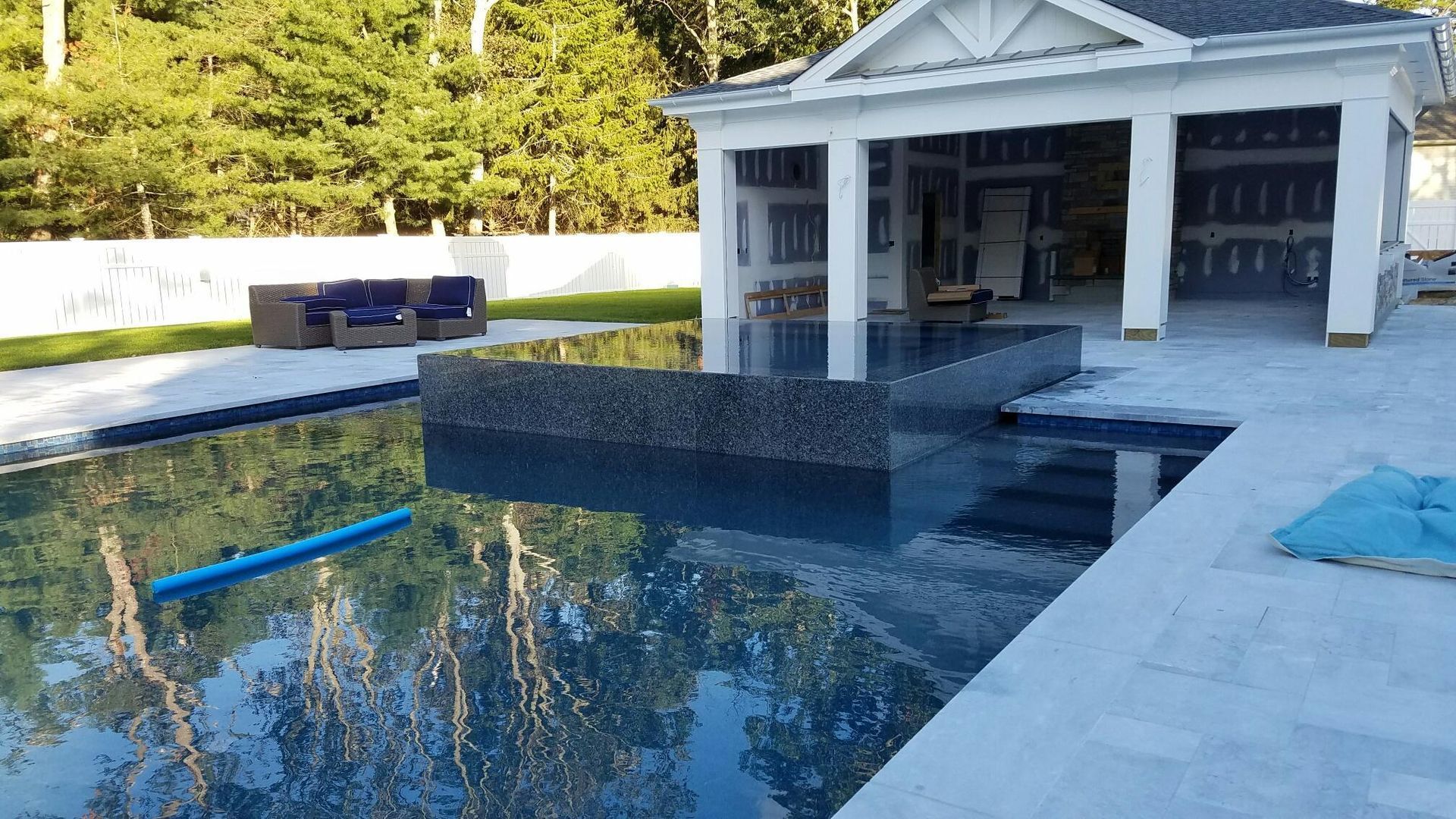 Pool with blue water and tiled edges, gazebo in the background, surrounded by trees.