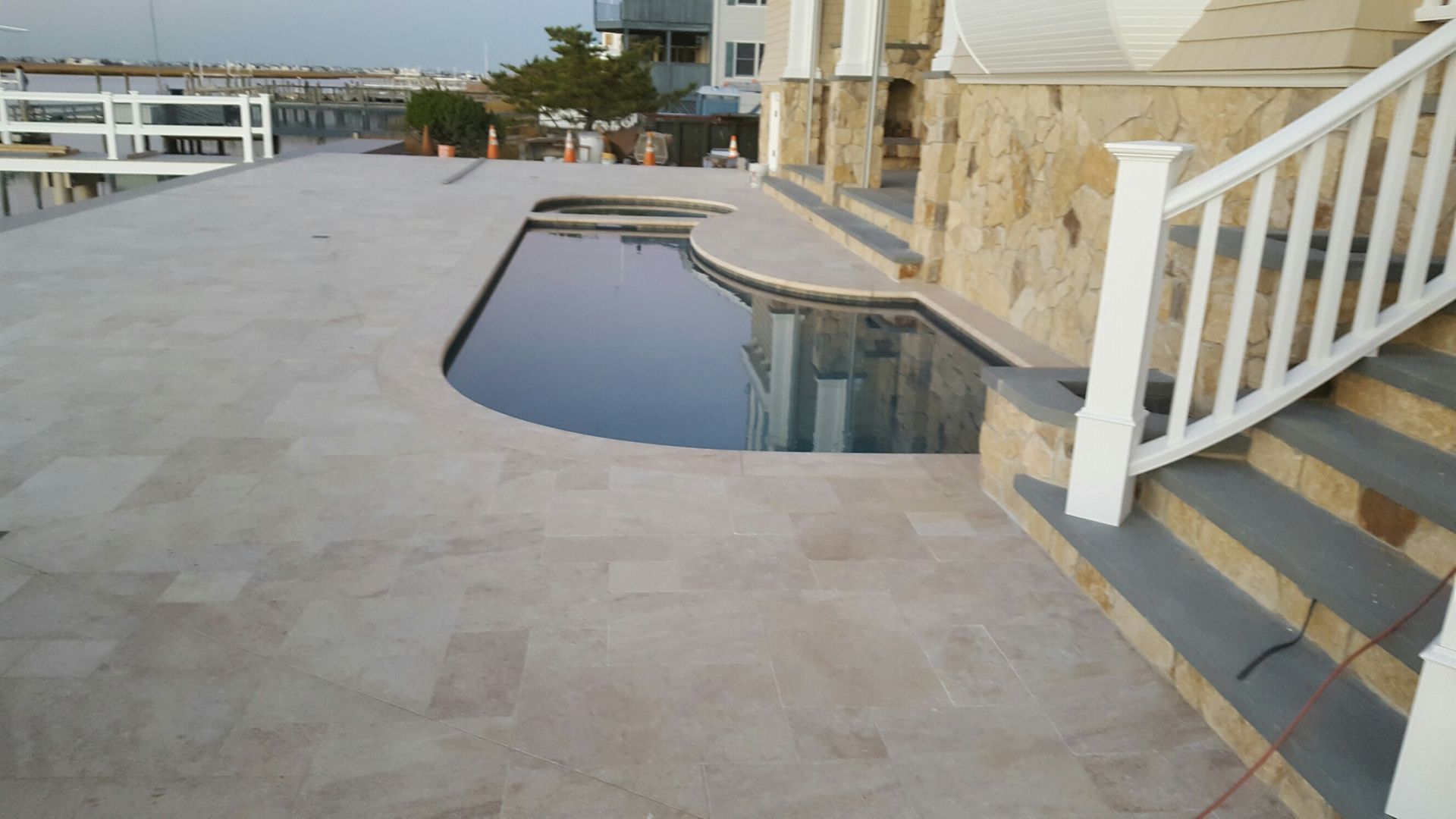 Poolside patio with pool, stone wall, and white railing.