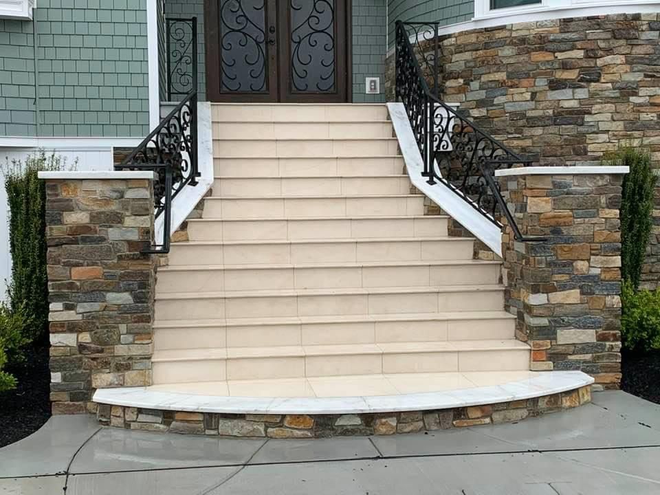 Stone-covered steps lead up to a double door. Wrought iron railings flank the stairs.