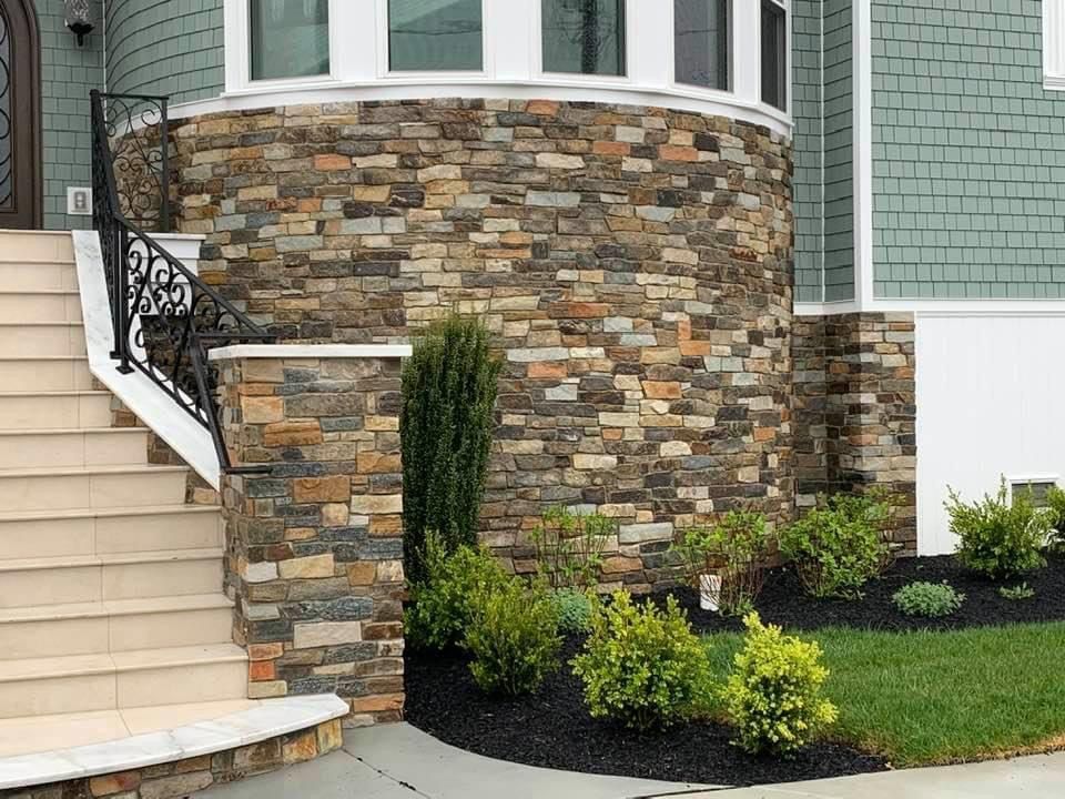 Stone facade of a house with steps and landscaping, featuring a curved wall and greenery.