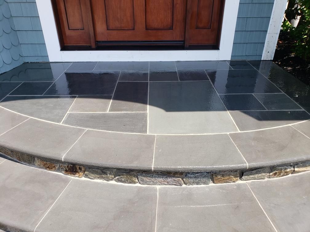 Slate-tiled front porch with a curved step leading to a brown wooden door under a blue-gray home exterior.