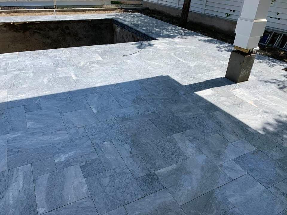 Gray stone patio with a sunken area and a white column, in sunlight.
