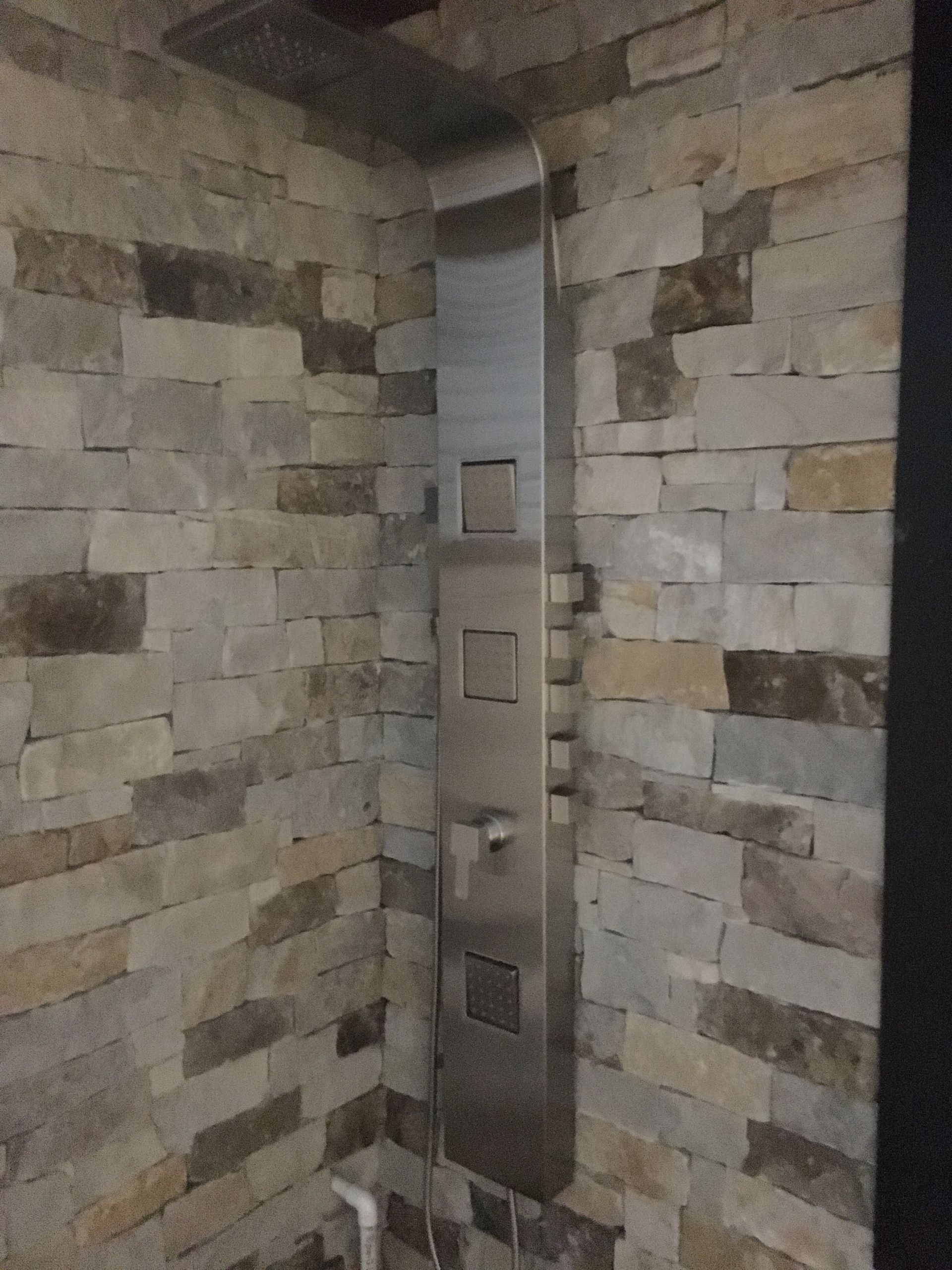 Shower panel with various spray heads, set against a stone wall.