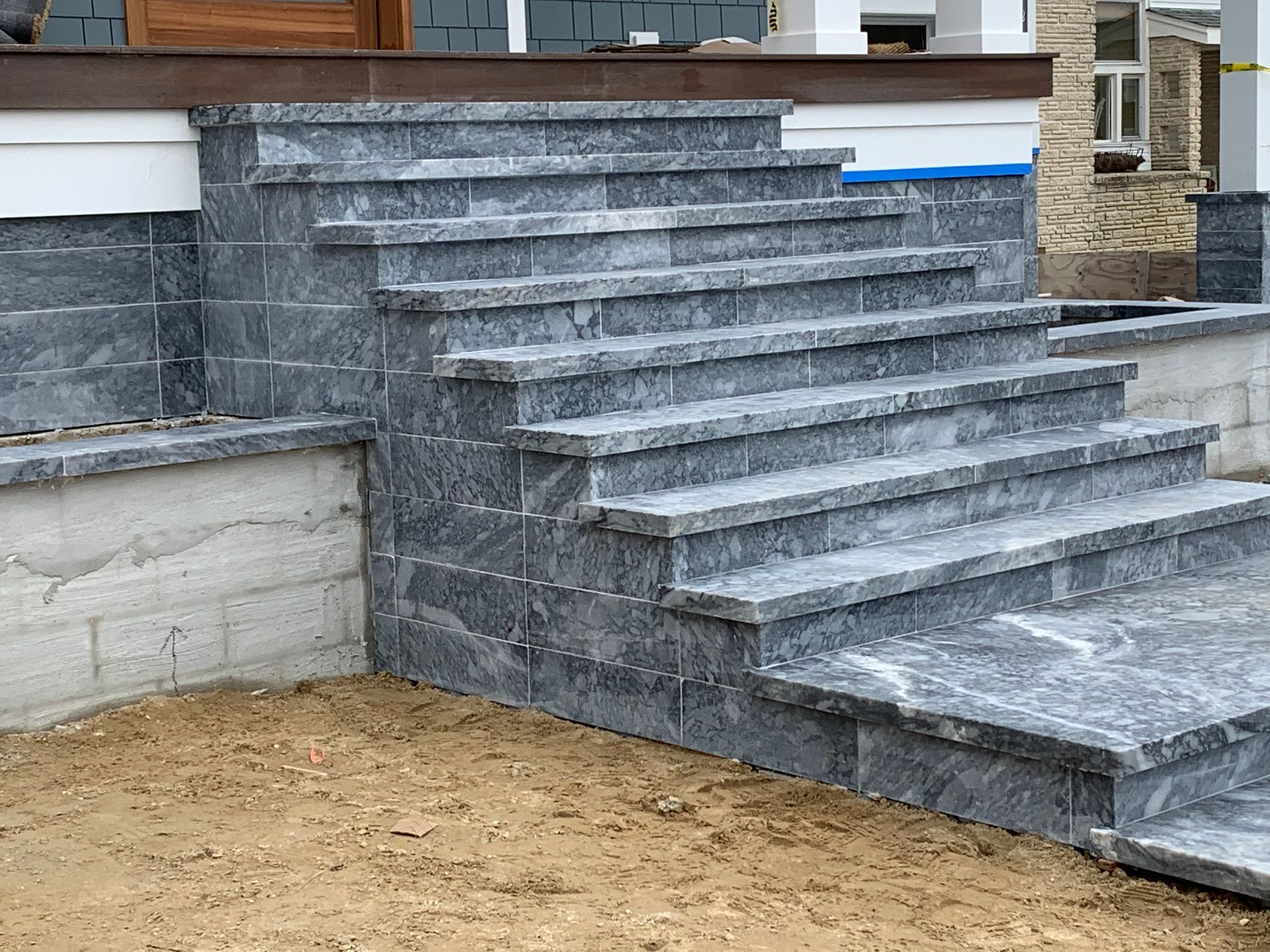 Gray stone steps leading to a building's entrance. The steps are constructed with stone blocks and have a concrete base.
