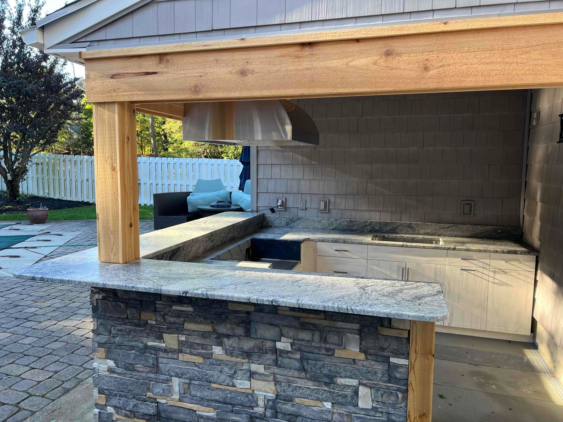 Outdoor kitchen with granite countertops, stone facade, and wooden supports.