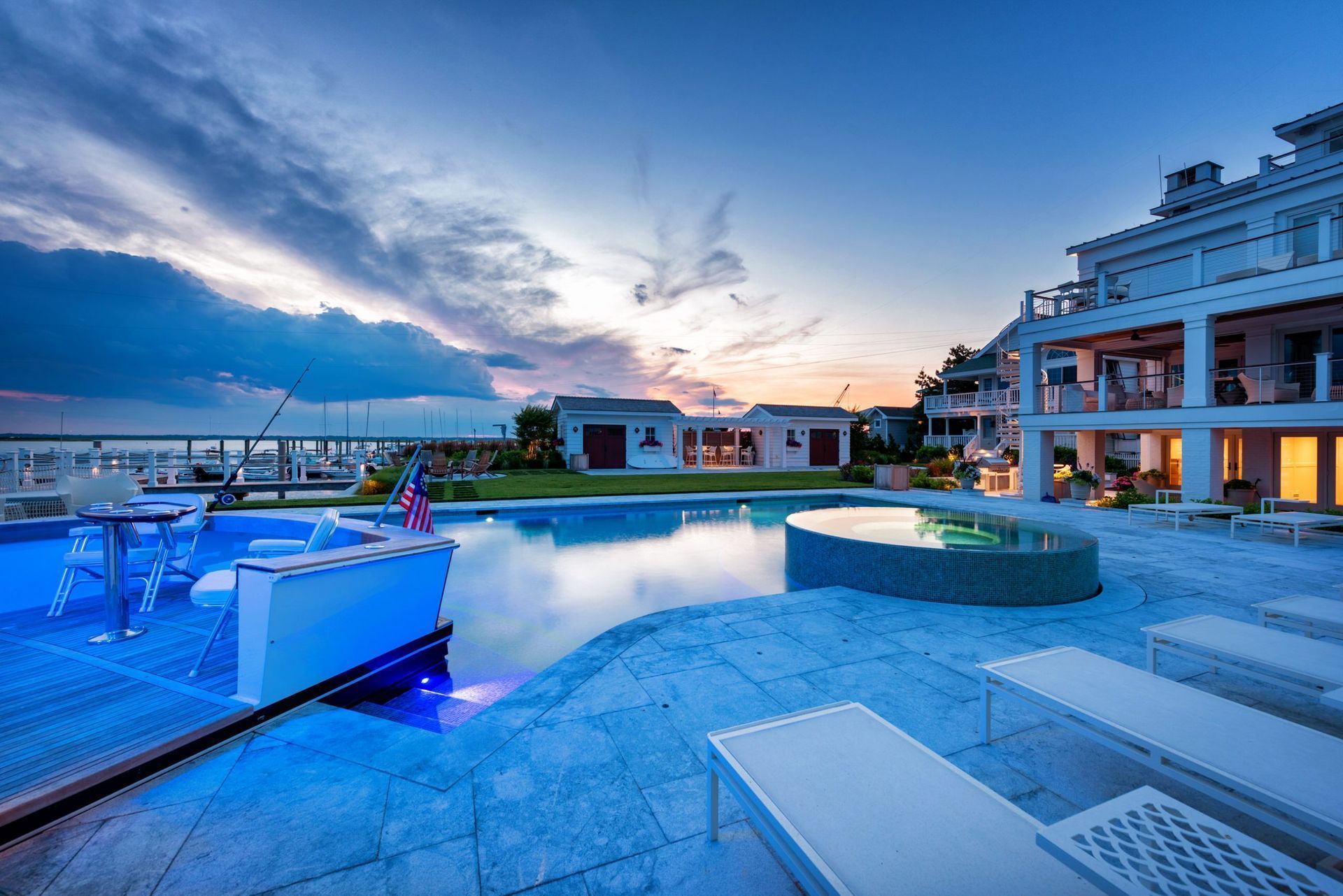 Luxury home with pool at sunset, blue and white hues. Sun loungers and water features.
