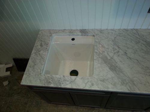 White bathroom sink set into a marble countertop, with dark cabinets below and white paneled wall behind.