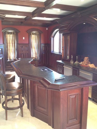 Dark wood bar in a room with arched windows, maroon walls, and a coffered ceiling.