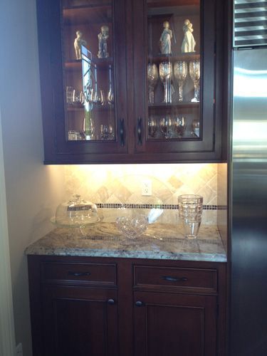 Dark wood cabinet with glass-front display case, countertop with decorative back splash, and under-cabinet lighting.