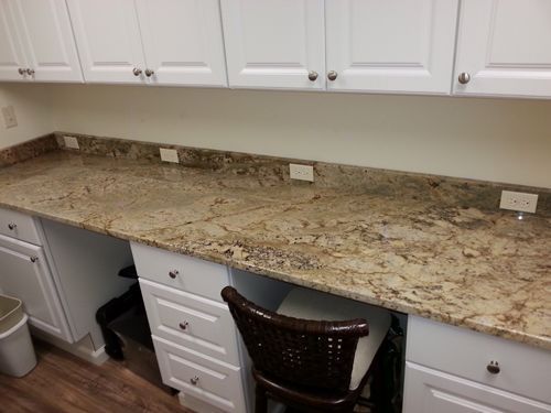 White cabinets and a granite countertop desk with a chair beneath it. Electrical outlets are in the countertop.