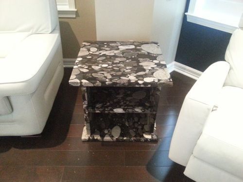 Granite-topped side table with two shelves, between two white leather chairs on a dark wood floor.