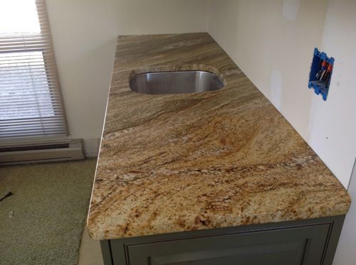 Granite countertop with sink, set on a gray cabinet. Room has beige walls, a window, and exposed electrical box.