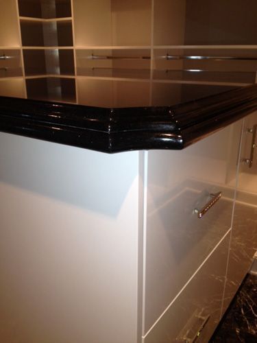 Black, glossy countertop with a decorative edge on white cabinets, possibly kitchen.