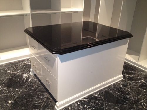 White closet island with a black countertop and silver drawer pulls.