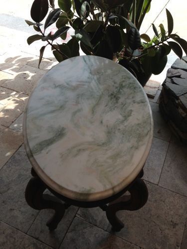 Round marble-topped table with green swirls, on dark wood legs, near leafy plant.