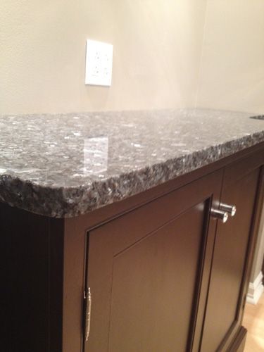 Dark granite countertop on a dark brown cabinet with silver hardware, against a tan wall with an outlet.