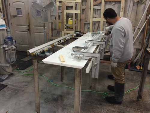 Person working on a white surface using clamps at a workshop table.