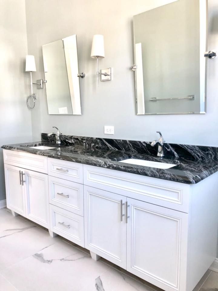 Bathroom with a white vanity, black countertop, two sinks, mirrors, and sconces.