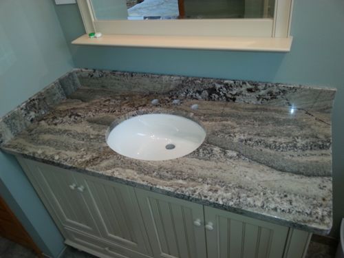 Bathroom vanity with granite countertop and oval sink. Light wood cabinet with matching mirror above.