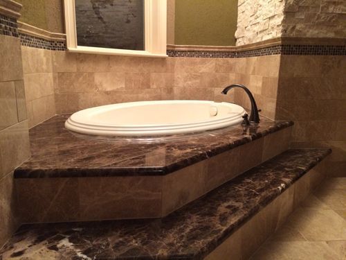 A built-in, oval bathtub surrounded by dark marble steps and tile in a bathroom.